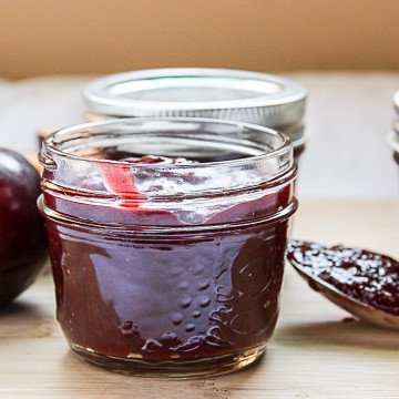 A jar of sauce with a plum on a table