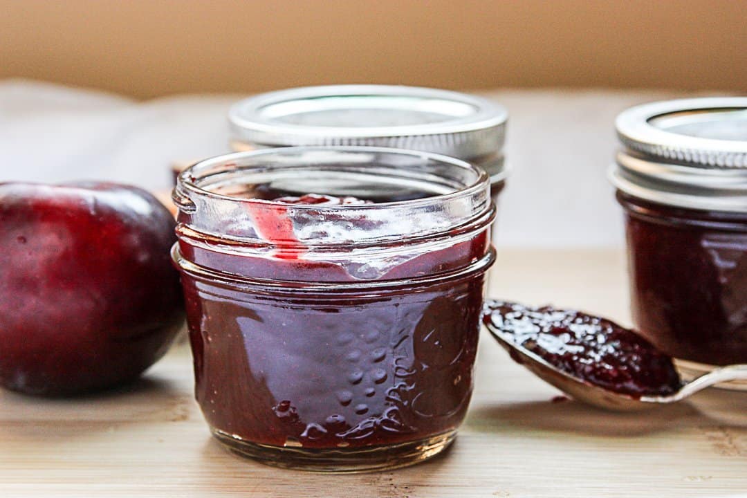 A jar of sauce with a plum on a table