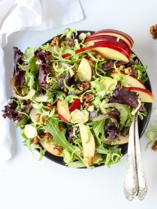 A top down view of shaved brussels sprouts and apple salad on a black plate with a fork.