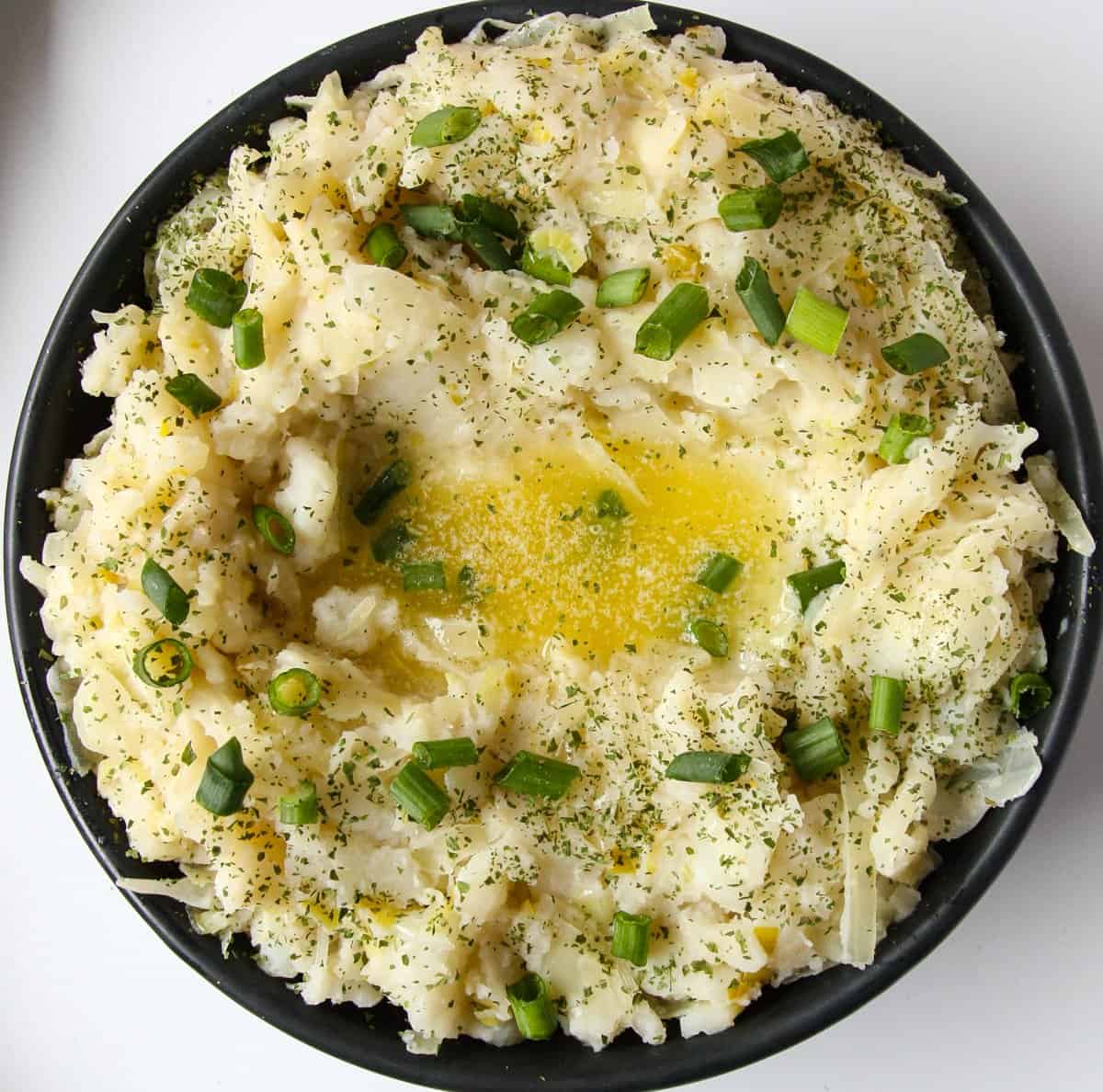 Irish Mashed Potatoes in a black bowl topped with melted butter.