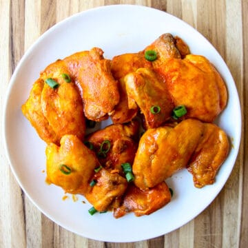 Chicken thighs on a white plate garnished with green onions.