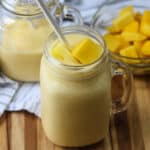 Two glasses of mango pineapple smoothie with white paper straws.