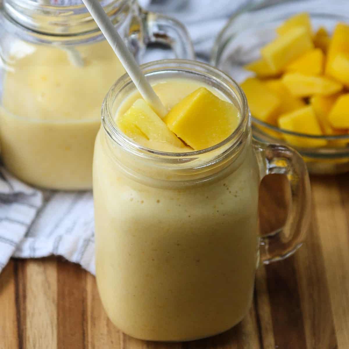Two glasses of mango pineapple smoothie with white paper straws.