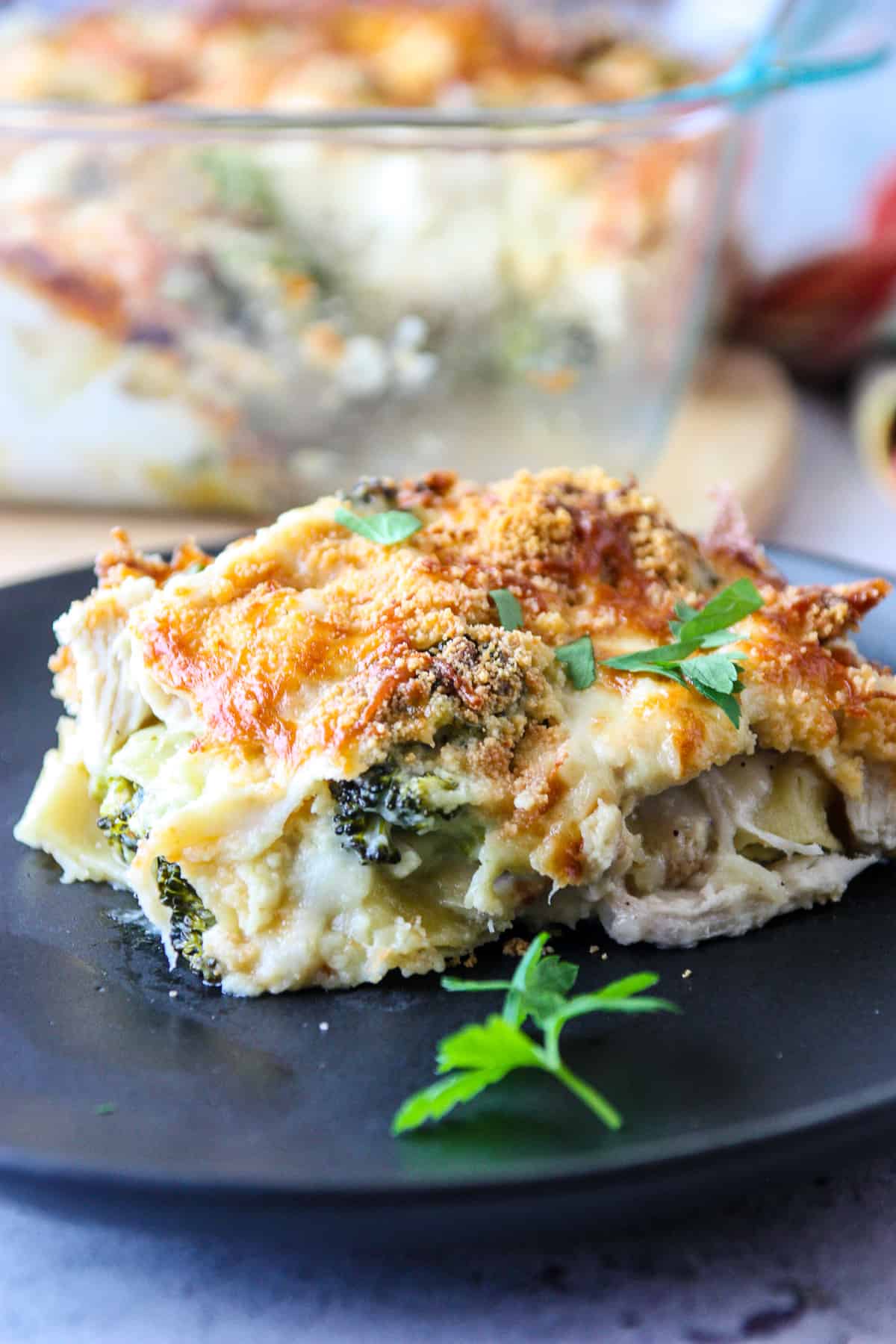 A slice of chicken broccoli lasagna on a black plate.