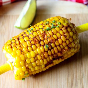 A piece of Cajun corn on the cob on a wooden board with corn shaped corn holders in either end.