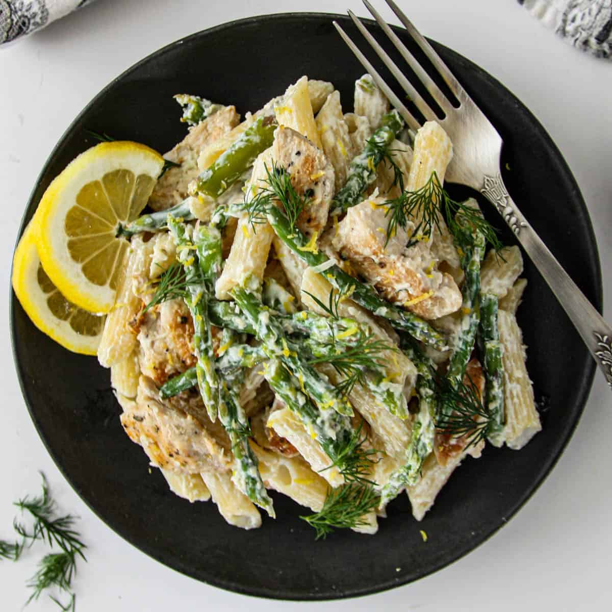 Asparagus and chicken pasta on a black plate.
